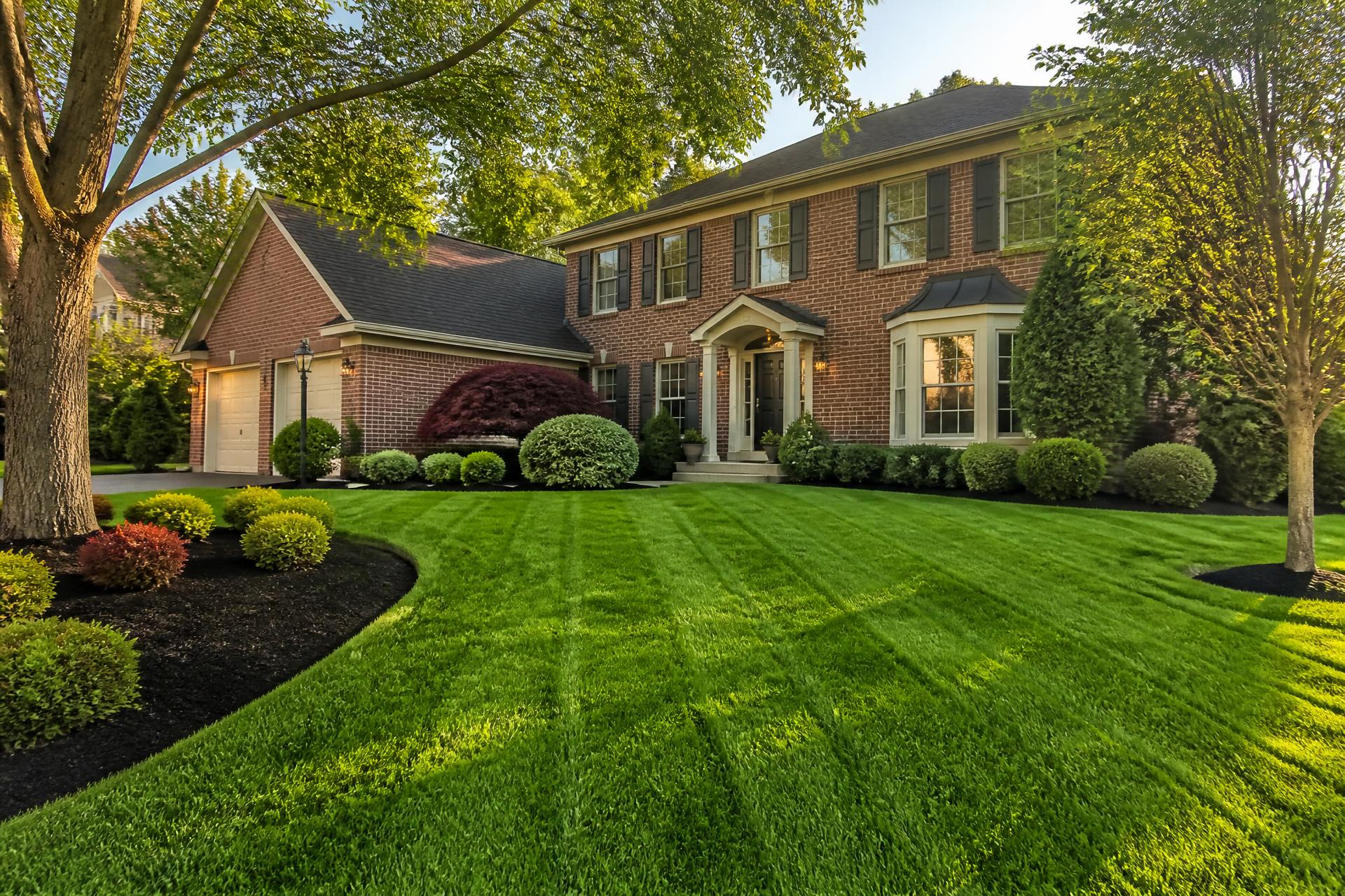 Manicured lawn and fresh landscape beds in front of a brick home